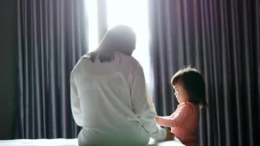 Asyalı anne yatak odasında kızıyla konuşuyor..
