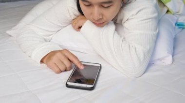 Asyalı kadın evde yatakta yatarken online alışveriş için akıllı telefon kullanıyor. Teknoloji ve rahatlama kavramı.
