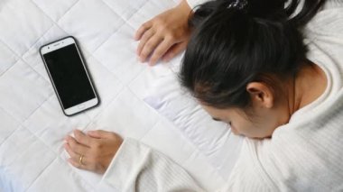 Geceleri elinde akıllı telefonla uyuyan Asyalı bir kadın. Teknoloji ve Sağlık Hizmetleri kavramı.