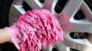 Köpüklü pembe eldiven tutan kadın araba lastiklerini yıkıyor..