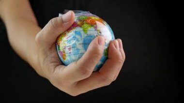 Kadın eli, dünyayı siyah arka planda plastik torba içinde tutuyor. Plastik molozların yol açtığı kirlilik nedeniyle küresel ısınma. Dünya Günü konsepti. 