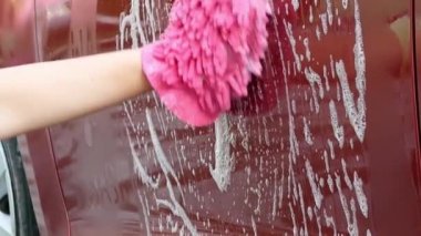 Araba yıkamak için köpüklü pembe eldiven tutan kadın..