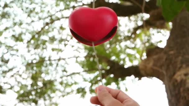 女人在花园里的树枝上挂着红色的心形陶瓷风铃 — 图库视频影像