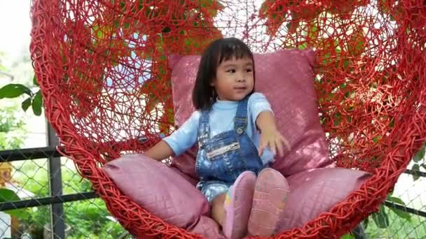 Adorable Happy Child Girl Sitting Red Wood Swing Chair Rattan — Stock Video