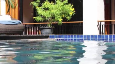 Odanın balkonundan havuz manzarasını görmek için beyaz perdeleri açın ve tatil köyünde yaz tatilinde dinlendirici sandalyeyi kullanın..