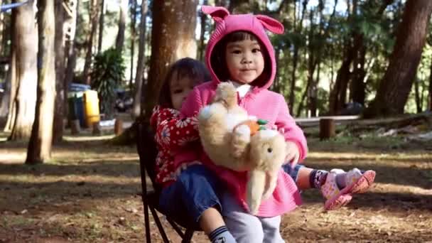 亚洲小女孩坐在椅子上和姐姐一起玩耍 和家人一起去松林野营 儿童户外活动与自然冒险的概念 — 图库视频影像