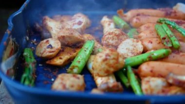 Tavada domuz eti, sosis, mantar ve baharatlı kuşkonmaz ızgara (Sichuan Pepper) ile anne eli. Asyalı aile çam ormanlarında kamp ateşinde yemek pişiriyor..
