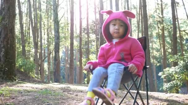 家族と一緒に松林でキャンプをしながら 椅子に座っているアジアの小さな子供の女の子 アウトドア活動と子供のための自然の中での冒険の概念 — ストック動画