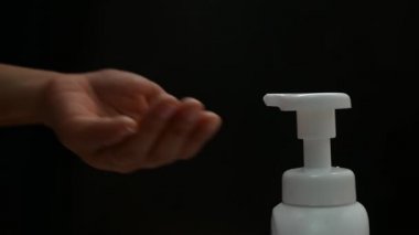 Kadının elini kapat beyaz plastik pompa şişesi ve diğer el daha temiz köpük al, siyah arka planda izole edilmiş. Cilt bakımı ürünü kavramı.