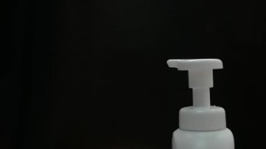 Kadının elini kapat beyaz plastik pompa şişesi ve diğer el daha temiz köpük al, siyah arka planda izole edilmiş. Cilt bakımı ürünü kavramı.
