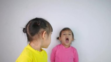 Mutlu gülümseyen Asyalı bir kızın portresi ve beyaz arka planda karamsar ablası..