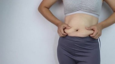Gri arka planda izole edilmiş aşırı miktarda göbek yağını çimdikleyen bir kadının eli. Koca göbekli kadın. Obezite ve Şişmanlık Konsepti.