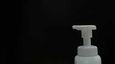 Kadının elini kapat beyaz plastik pompa şişesi ve diğer el daha temiz köpük al, siyah arka planda izole edilmiş. Cilt bakımı ürünü kavramı.