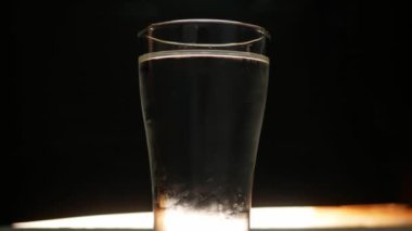 El 'in, siyah arka planda izole edilmiş su dolu bir bardağa buz attığı yakın plan..