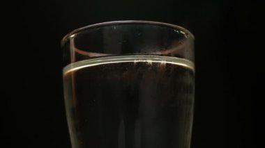 El 'in, siyah arka planda izole edilmiş su dolu bir bardağa buz attığı yakın plan..