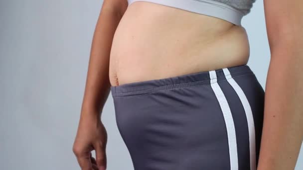 灰色の背景に隔離された過度の腹の脂肪をつまむ女性の手のクローズアップ 女性の脂肪腹 肥満と太りすぎの概念 — ストック動画