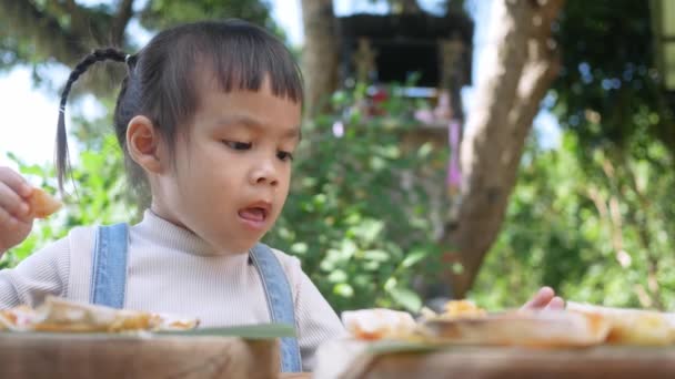 かわいい空腹の子供の女の子は裏庭で自家製のピザを食べることを楽しむ 屋外のランチテーブルで家族と一緒に小さな女の子 選択的焦点 — ストック動画