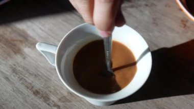 Sabahları ahşap masada kaşıkla kahveyi karıştıran kişinin üst görüntüsü..