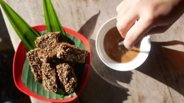 Kahveyi kaşıkla karıştıran ve kahvaltı için ahşap masada granola çubukları olan birinin üst görüntüsü..