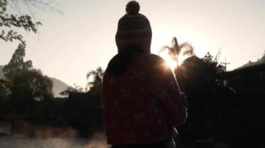 Mutlu güzel kadının silueti güneşin doğuşunda soğuk havanın tadını çıkarıyor..