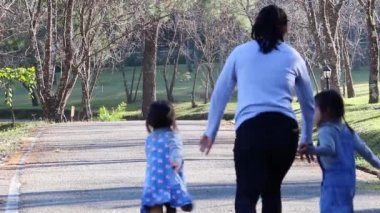 Asyalı aile dışarıda parkta rahat rahat oturuyor. Ebeveyn ve çocuk bahçede yürüyüşe, koşmaya, oynamaya ve etkinlik yapmaya gidiyorlar..
