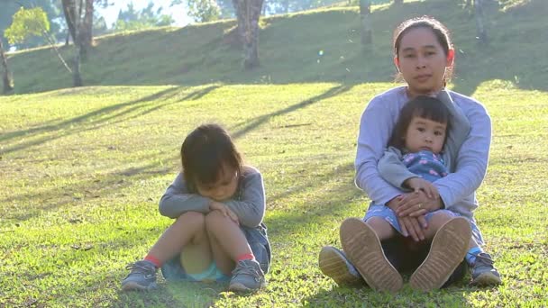 母親に無視され 母親と妹の近くの芝生の上に座っている小さなアジアの子供の少女の肖像画 子どもの表情や感情の概念は — ストック動画