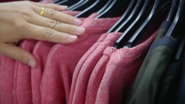 女性の手は服のラックの間で実行し セーターを選択します — ストック動画