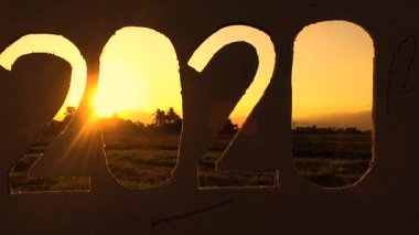 Günbatımında gökyüzü arkaplanı üzerinde 2020 metin olan geri dönüşüm kartonu silueti ve metinde gün ışığı. Yeni Yıl ve Kutlama Kavramları.