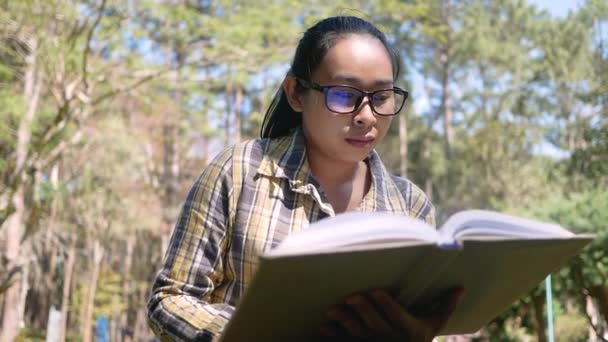 アジアの若い女性が夏の日に公園に座って本をリラックスして読んでいます ライフスタイルコンセプト — ストック動画