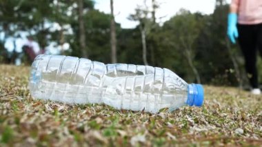 Eldivenli gönüllülerin eli parktaki çimlerden plastik bir şişe alıyor. Çevreyi kurtarma ve plastik kirliliğini durdurma kavramları.