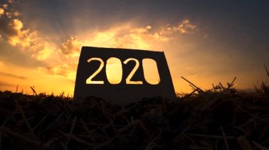 Günbatımında gökyüzü arkaplanı üzerinde 2020 metin olan geri dönüşüm kartonu silueti ve metinde gün ışığı. Yeni Yıl ve Kutlama Kavramları.