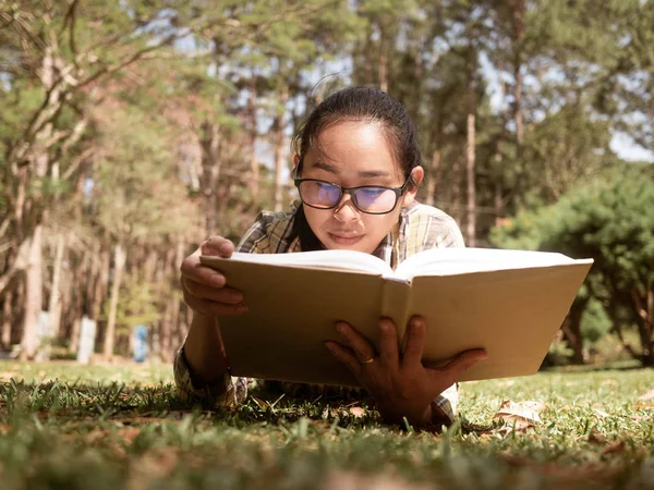 Jovem mulher asiática relaxamento e ler um livro deitado na grama i — Fotografia de Stock