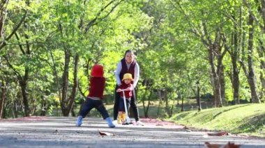 Genç bir anne, kızına yaz parkında scooter sürmeyi öğretiyor. Mutlu aile ve çocukluk kavramı.