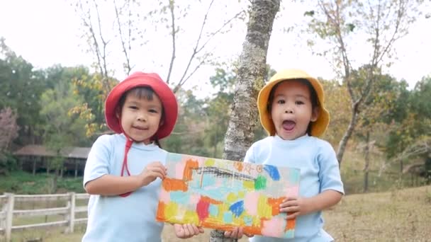 Dwie Szczęśliwe Dziewczynki Pokazujące Swoje Kolorowanki Kartonowym Pudełku Recyklingu Ogrodzie — Wideo stockowe