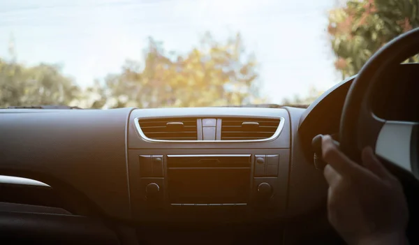 Driver\'s hand on the black steering wheel with dashboard inside