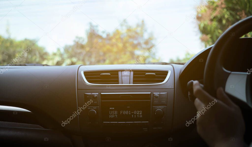 Driver's hand on the black steering wheel with dashboard inside 