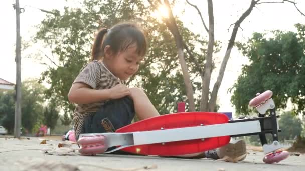 Χαριτωμένο Ασιατικό Κοριτσάκι Κάθεται Στο Έδαφος Αφού Έπεσε Από Σκούτερ — Αρχείο Βίντεο