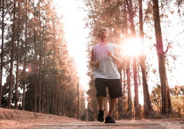 Asijské senior muž jogging v parku přes západ slunce nebe pozadí. — Stock fotografie