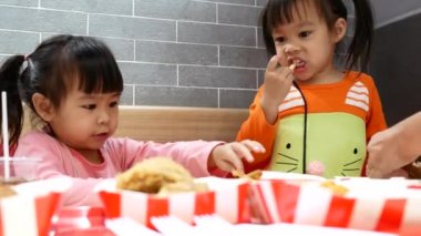 Asyalı küçük kız kardeşler, ailesiyle birlikte kızarmış tavuk, patates kızartması ve nektarın tadını çıkarıyorlar. KFC dünyaca ünlü bir Amerikan fast food restoranıdır. Sağlık kavramı.