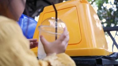Dışarıdaki kafedeki geri dönüşüm kutusuna plastik içecek bardağı atan sevimli küçük kız. Dünyayı kurtarma kavramı. Sıfır atık.