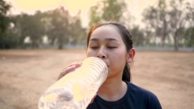 Parkta koştuktan sonra plastik şişelerden su içen Asyalı genç bir kadın. Kilo ver. Sağlıklı yaşam tarzı kavramı.