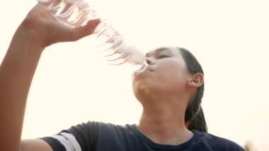 Parkta koştuktan sonra plastik şişelerden su içen Asyalı genç bir kadın. Kilo ver. Sağlıklı yaşam tarzı kavramı.