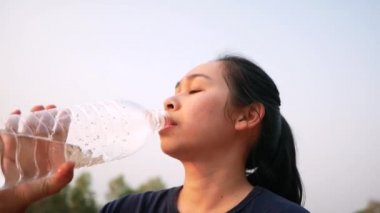 Parkta koştuktan sonra plastik şişelerden su içen Asyalı genç bir kadın. Kilo ver. Sağlıklı yaşam tarzı kavramı.