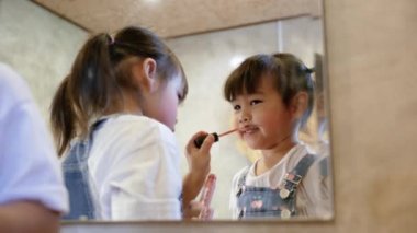 Makyaj yapan ve odadaki aynada eğlenen sevimli küçük kız..