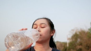 Parkta koştuktan sonra plastik şişelerden su içen Asyalı genç bir kadın. Kilo ver. Sağlıklı yaşam tarzı kavramı.
