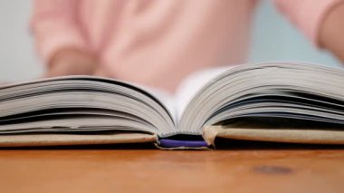 Genç bir kadın bir kitabın sayfalarını çeviriyor ve kütüphanede okurken parmaklarını sayfa boyunca hareket ettiriyor. Seçici odak.