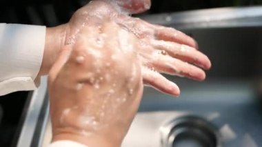 Kadın lavaboda akan suyun altında ellerini sabunla yıkıyor. Hijyen ve sağlık hizmetleri kavramı.
