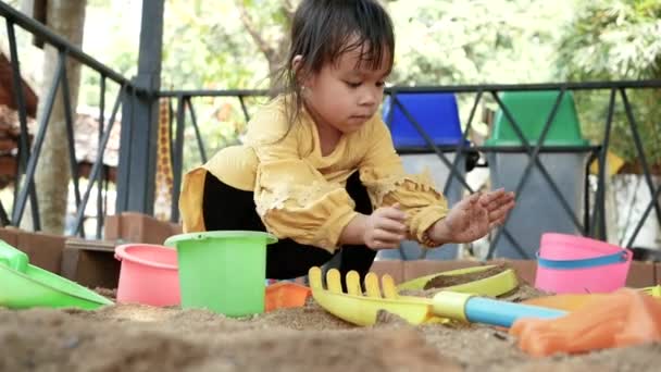 在阳光灿烂的夏日 快乐的小女孩坐在沙盒里玩塑料玩具 — 图库视频影像