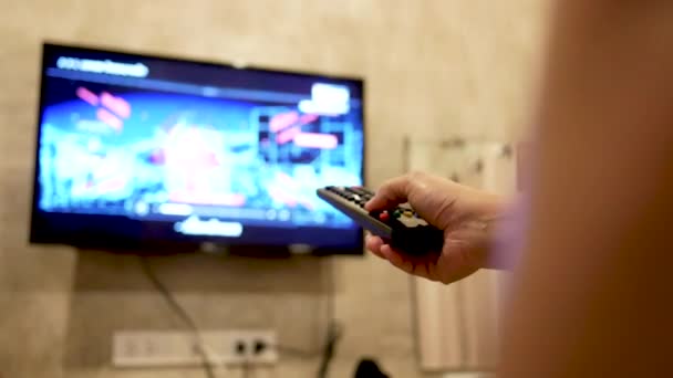 部屋でテレビを見ているアジアの若い女性は 音量を調節したり テレビチャンネルを変更したりするために手をリモートコントロールしています リビングルームでのリラクゼーション 選択的焦点 — ストック動画