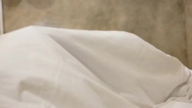 Genç anne ve kızları yatak odasında peekaboo oynayarak eğleniyorlar. Mutlu aile yatakta beyaz battaniyenin altında oynuyor. Mutlu aile ve çocukluk kavramı.